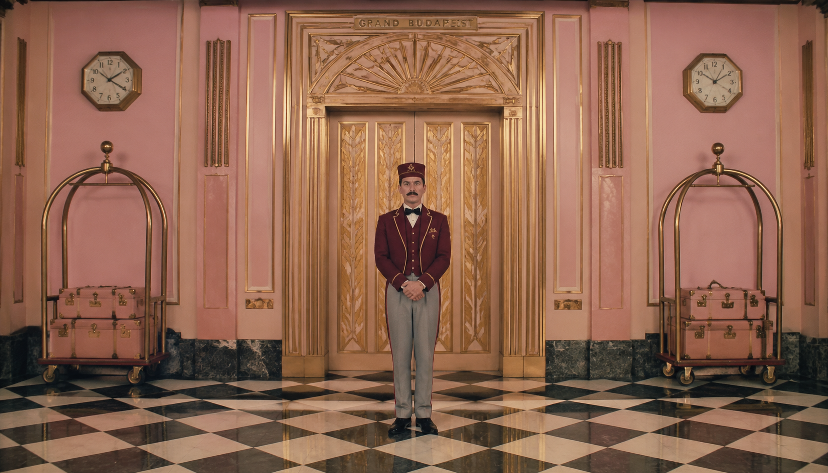 An Art Deco hotel concierge stands in a carefully balanced pastel interior.