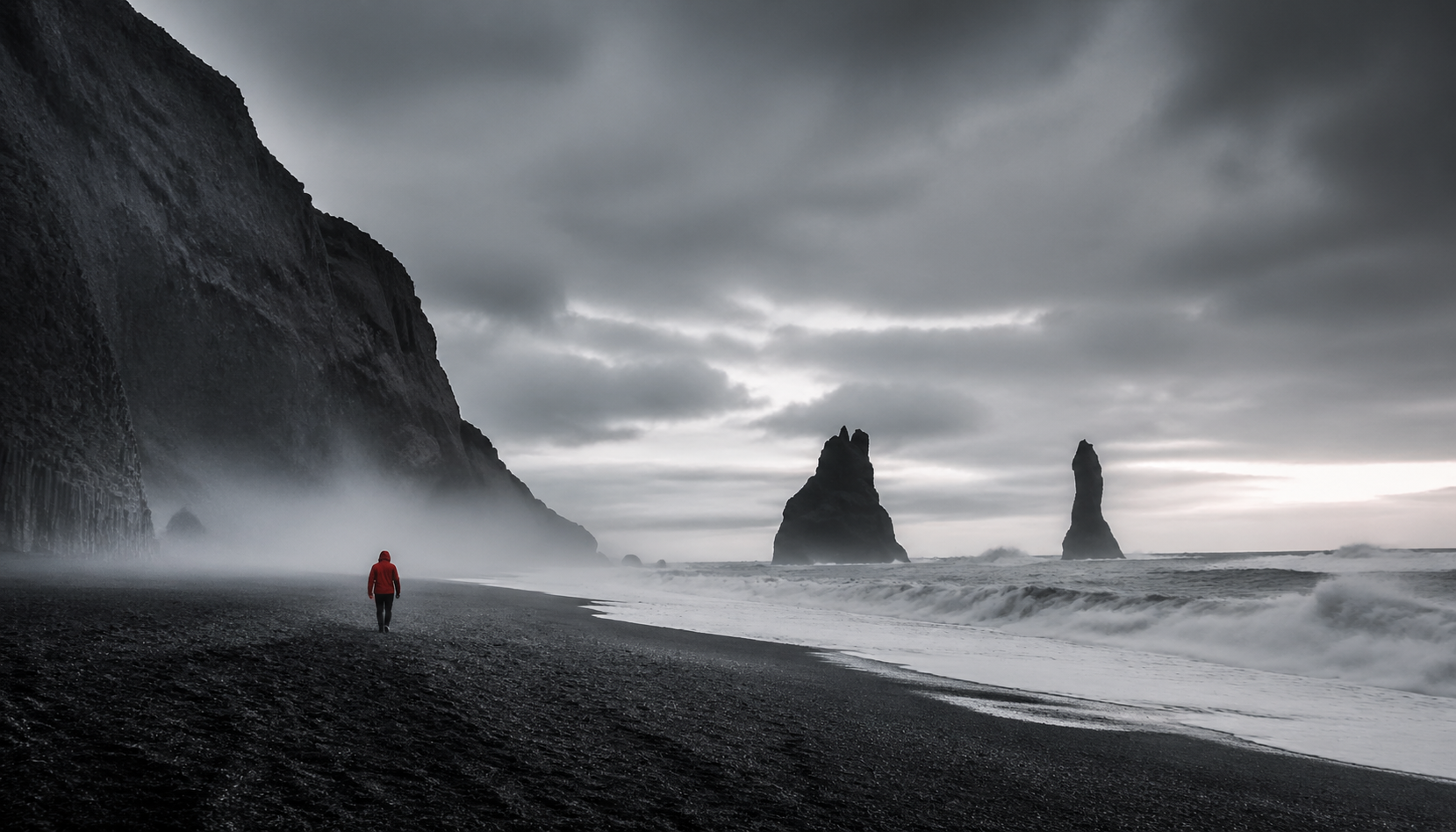 Basalt sea stacks and dark waves contrast with a small red visual accent.